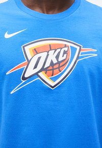 Μπλε πουκάμισο με μεγάλο λογότυπο του μπασκετικού Oklahoma City Thunder και λευκό λογότυπο Nike στο πάνω αριστερό μέρος του στήθους.