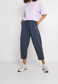 Ljuslila kortärmad t-shirt i cropped-stil, ihopparad med mörkblå, löst sittande, ankellånga sweats. Skorna har pastellfärger.