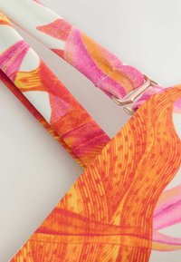 Sangle textile réglable avec imprimé abstrait rose, orange et blanc et coulisse métallique dorée sur tissu à motif.