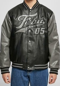 Svart läderbomberjacka med grå ärmar, som har en framträdande logotyp, tryckknappar och randiga ribbade ärmslut och nederkant.