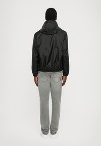 Svart lätt jacka med ståkrage, elastiska ärmslut och en åtsittande nederkant, kombinerad med grå jeans och vita sneakers.