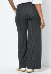 Pantalons larges à rayures noires en tissu doux, dotés d'une taille haute et de deux poches arrière. Associés à des baskets blanches.