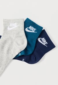 Drei Paar Knöchelsocken in Grau, Türkis und Marineblau, mit geripptem Muster und weißen Nike-Logos an den Bündchen.
