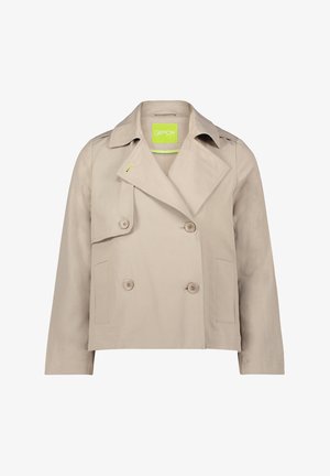 Veste beige à double boutonnage avec col pointu, poches latérales et étiquette logo verte. Fabriquée en tissu lisse avec une forme légèrement structurée.