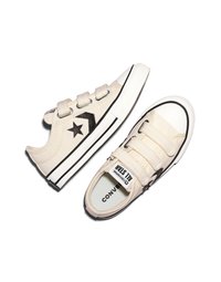 Μπεζ πάνινα παπούτσια χαμηλού πατούμενου με μαύρο λογότυπο αστέρι, λευκές λαστιχένιες μύτες και τρεις ιμάντες βέλκρο, εμφανιζόμενα από πλευρική και κορυφαία όψη.