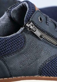Sneaker blu navy con tomaia in pelle testurizzata, sezioni in rete, zip laterale e suola in gomma marrone; presente dettagli del logo in rilievo.