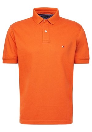 Pomarańczowa koszulka polo z krótkim rękawem, zapinana na dwa guziki, z małym logo Tommy Hilfiger na lewej piersi.