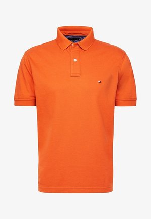 Pomarańczowa koszulka polo z krótkim rękawem, zapinana na dwa guziki, z małym logo Tommy Hilfiger na lewej piersi.