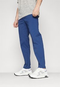 Blue pants made of lightweight fabric, featuring a straight leg design, paired with white sneakers highlighting a mesh pattern and black accents.