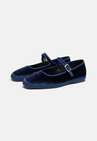 Zapatos de terciopelo azul marino con puntera redondeada, una correa con hebilla de metal y borde trenzado. Suela plana con una textura suave.