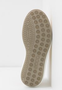 Semelle de chaussure avec motifs circulaires antidérapants de tailles variées, de couleur beige, comportant le nom de la marque « ecco » embossé sur la semelle.