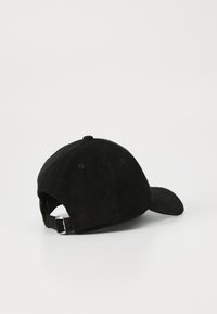 Casquette de baseball en velours côtelé noir avec boucle en métal ajustable à l'arrière, reposant sur une surface blanche.