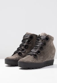 Le sneakers con zeppa in suede grigio presentano lacci in satin neri passati attraverso occhielli circolari, suole in gomma testurizzata e una punta rotonda liscia.