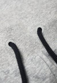 Tela gris texturizada con cordón negro oscuro, con ojales grises. Enfoque en los detalles de la costura y el tejido.