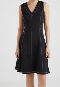 Abito nero senza maniche con scollatura a V, caratterizzato da cuciture bianche a contrasto e gonna svasata, realizzato in tessuto morbido ed elastico.