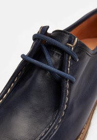 Chaussure en cuir navy avec finition texturée, dotée d'un bout rond, de coutures contrastées et de lacets bleu marine tressés. Semelle marron visible.