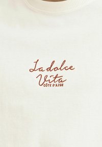 Hvit bomullssweatshirt med brunt brodert tekst "La dolce Vita CÔTE D'AZUR" på forsiden. Rund hals og myk tekstur.