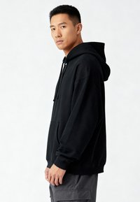 Sudadera negra con capucha, bolsillo delantero, ajuste holgado, puños acanalados y capucha con cordón, usada por una persona vista de perfil.