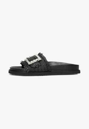 Black woven slide sandal featuring a textured upper, large crystal-embellished buckle, and flat rubber sole. Simple, open-toe design.