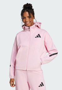 Felpa con zip di colore rosa chiaro, dotata di cappuccio, con strisce nere sui maniche e logo nero sul petto. Tessuto morbido.