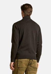 Maglione nero a maglia con collo alto, polsini e orlo a coste. Cuciture dettagliate sulle spalle, abbinato a pantaloni cargo verdi oliva.