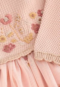 Tissu tricoté rose avec broderie florale texturée en jaune doux, crème et rose, associé à un tissu tulle rose transparent et fluide en dessous.