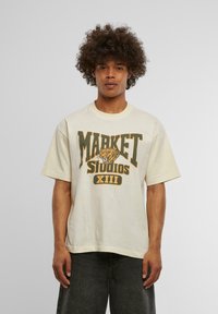 Krémové bavlněné tričko s velkým grafikou "MARKET STUDIOS XIII" v zelené a oranžové barvě, s ilustrací tygra.