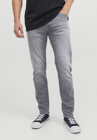 Vaqueros de mezclilla gris con un ajuste slim, que presentan un diseño clásico de cinco bolsillos. Usados con zapatillas negras y una camiseta negra, mostrando una textura sutil.