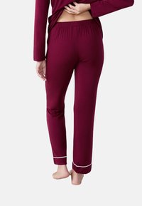 Bordeaux pyjamabroek van zacht materiaal, met een elastische tailleband en witte afwerking bij de manchetten, aansluitende stijl en enkel lengte.