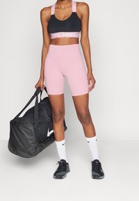 Czarny stanik sportowy z różową opaską "Nike Pro", różowe spodenki z wysokim stanem, czarne buty sportowe, białe skarpetki i czarna torba sportowa z logo.