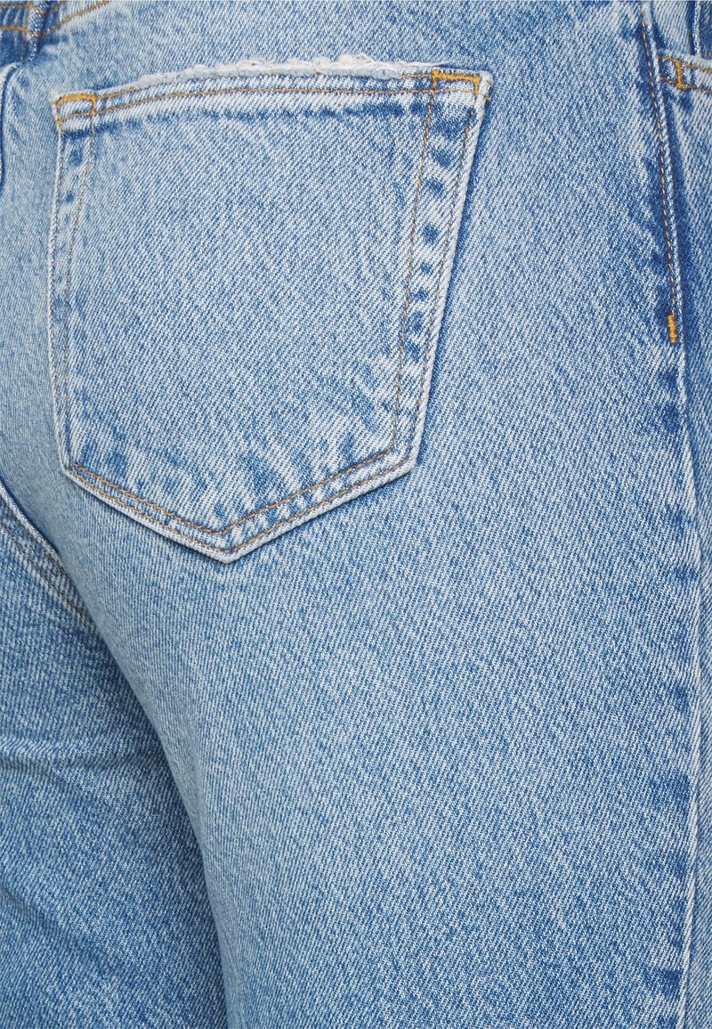 Helleblaue Jeans aus Denim verfügen über eine Gesäßtasche mit Nahtdetails und einer leicht abgenutzten Textur. Der Stoff zeigt ein schwaches diagonales Muster.