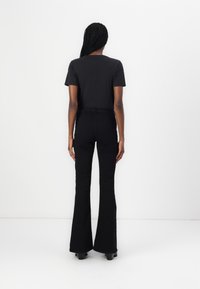 Black t-shirt paired with high-waisted black flared trousers. Smooth fabric, minimal design, fitted silhouette, and straight leg opening.