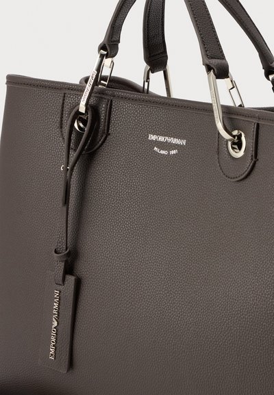 Τσάντα tote Emporio Armani από δέρμα σκούρου καφέ με υφή, με ασημένια μεταλλικά χερούλια και δερμάτινη ταμπέλα με την επωνυμία που κρέμεται από το χερούλι.