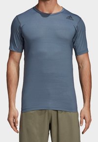 Koszulka sportowa z krótkim rękawem w jasnym niebieskim kolorze, wykonana z materiału odprowadzającego wilgoć z teksturowanym wzorem; posiada logo Adidas na klatce piersiowej.