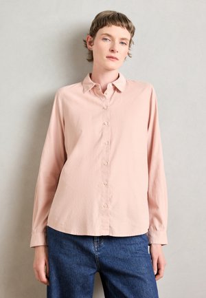 Chemise à manches longues rose clair avec un col et un bouton sur le devant. Tissu doux et texturé, avec une coupe décontractée et un ourlet rentré.
