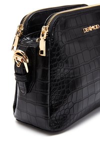 Sac à main noir en cuir gaufré crocodile avec quincaillerie dorée, fermetures éclair doubles et une forme structurée. Fini texturé et logo prominent.