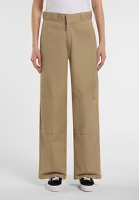 Khaki vida-byxorna med hög midja, tillverkade av slitstarkt tyg, med horisontella söms accentuerade och fickor. I kombination med svarta skor.