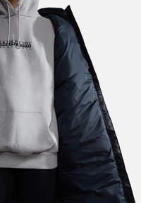 Grijze sweatshirt met capuchon, voorzien van een centraal logo, gecombineerd met een zwarte, glanzende pufferjas met voering. Beide hebben een relaxte pasvorm.