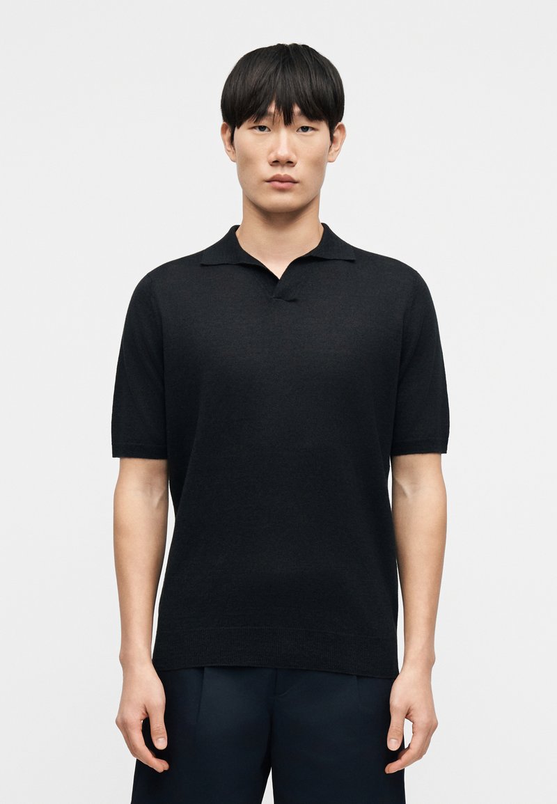 Polo noir à manches courtes avec un col classique. Confectionné dans un matériau lisse et léger, avec un design simple et épuré.