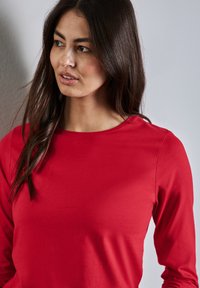 Rotes Langarmshirt aus weichem, leichtem Stoff; mit Rundhalsausschnitt und schmalen Ärmeln. Glatte Textur ohne sichtbare Muster.