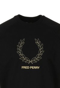 Zwarte trui met ronde hals, voorzien van een gouden lauwerkrans en de tekst "FRED PERRY" geborduurd op de voorkant. Gemaakt van katoen.