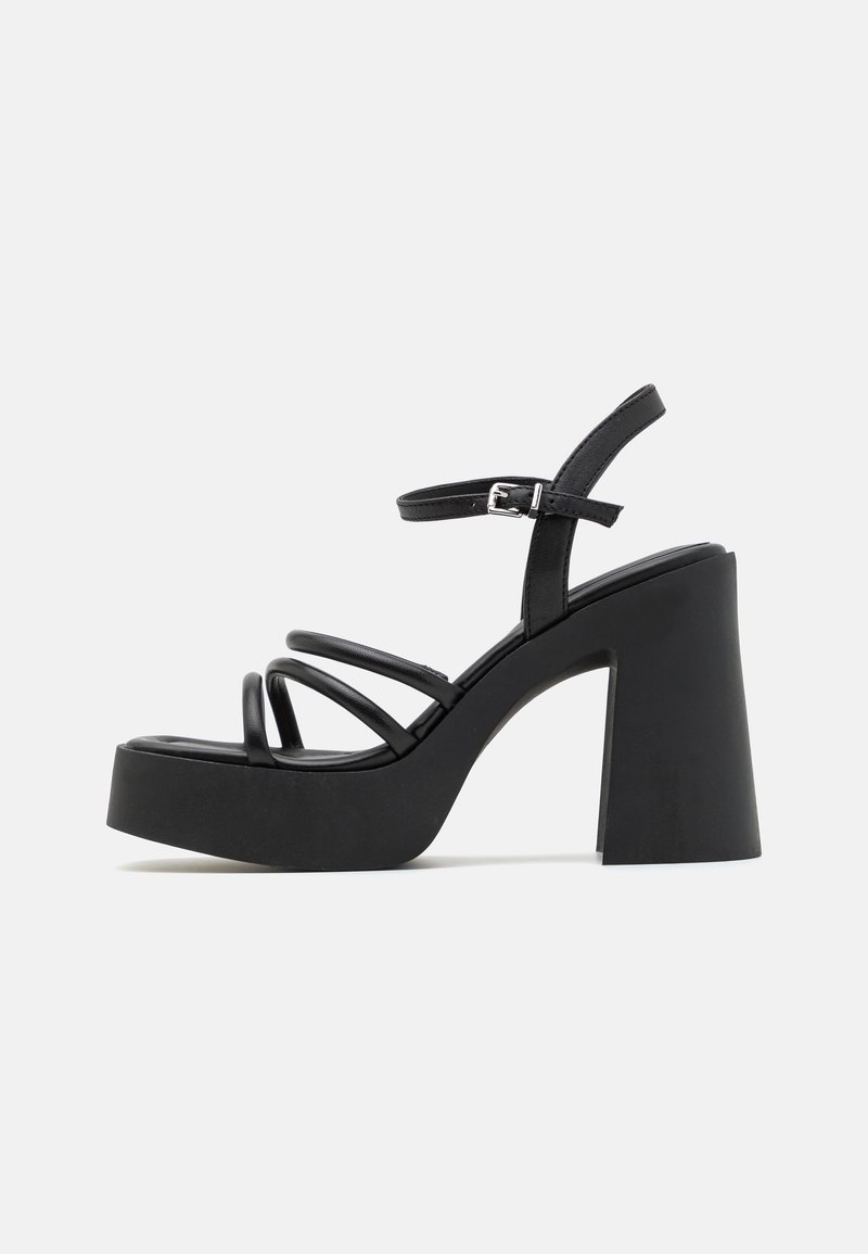Sandale à talons hauts noire à plateforme avec un chunky block heel, de fines sangles frontales multiples, et une sangle de cheville avec boucle en argent sur fond blanc.