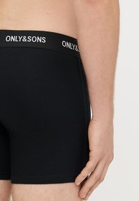 Mustad puuvillased bokserid pehme elastse vöökohaga, millel on valgete tähtedega "ONLY & SONS". Kangas tundub sile ja keha järgiv.
