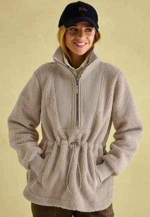 Beiger Fleece-Pullover mit hohem Kragen, geripptem Einsatz, Reißverschluss und verstellbarem Zugband in der Taille. Verfügt über seitliche Taschen und eine weiche Textur.