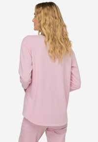 Lichtroze blouse met lange mouwen, een relaxed fit, ronde halslijn en zachte textuur. Achterkant met een lichte afgeronde zoom en opgerolde mouwen.