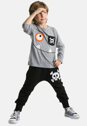 Graues Langarmshirt mit Monster-Gesicht-Design und schwarze Hose mit weißem Schädeldruck. Das Outfit wird durch graue Sneakers ergänzt.