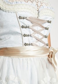 Vêtement bleu clair avec détails en dentelle et satin, liens en ruban de satin, éléments décoratifs en argent et surjupe brodée.