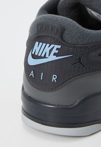 Nike Air sneakers har en overdel i sort læder med en struktureret overflade, blå logo detaljer og en tyk grå sål.