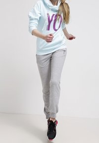 Sudadera azul clara con un gran texto púrpura "YO", combinada con pantalones de chándal grises y zapatillas deportivas negras con detalles en rosa.