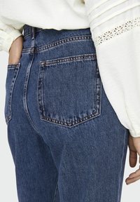 Högmidjade blå denim jeans har en klassisk femficksdesign, orange sömmar och en lätt textur. Bakhandsfickornas placering är standard.